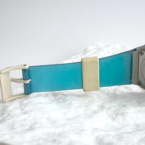 May include: A Casio watch with a translucent blue strap, a cream-colored buckle, and a cream-colored strap keeper. The stainless steel back of the watch case is visible, featuring the text Casio, FS-01, Stainless Steel Back, and Water Resistant.