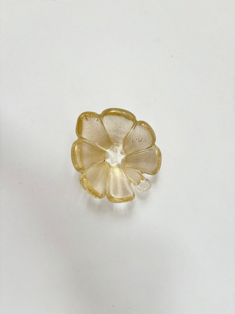 May include: A gold-colored glass dish shaped like a flower with five petals.