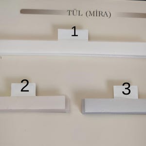 Puede incluir: Primer plano de tres barras de cortina rectangulares blancas con etiquetas numeradas 1, 2 y 3. El texto "T&Uuml;L (MIRA)" est&aacute; en la parte superior. Las barras est&aacute;n montadas en una pared clara.