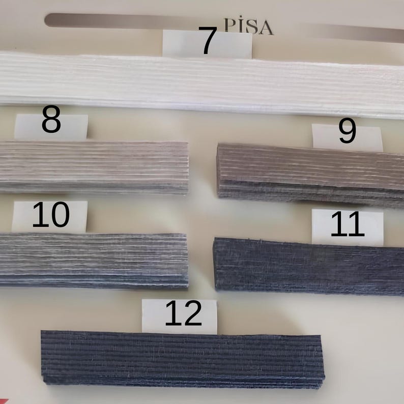 Puede incluir: Una colecci&oacute;n de muestras rectangulares texturizadas en varios tonos de gris y azul. Las muestras est&aacute;n dispuestas horizontalmente, con etiquetas numeradas del 7 al 12. La palabra "PISA" est&aacute; impresa encima de la muestra 7. Las muestras parecen ser muestras de tela o material.