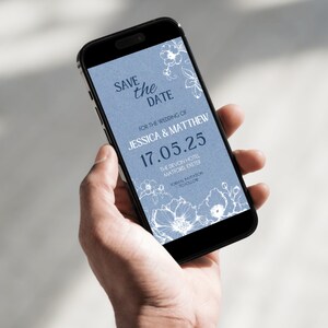 May include: A blue and white save the date card on a smartphone screen. The card features a floral design and the text "Save the Date" for the wedding of Jessica & Matthew on 17.05.25 at The Devon Hotel, Matford, Exeter. Formal invitation to follow.