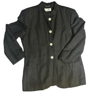 Könnte beinhalten: Ein dunkelbrauner Blazer mit Stehkragen und vier weißen Knöpfen. Der Blazer hat zwei Vordertaschen und lange Ärmel. Der Stoff scheint Leinen oder eine Leinenmischung zu sein.