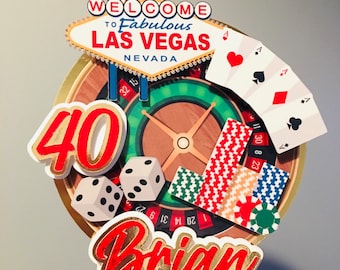 May include: A cake topper featuring a Las Vegas theme with a roulette wheel, playing cards, dice, and the text "WELCOME TO Fabulous LAS VEGAS NEVADA" and "40 Brian".
