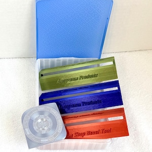 May include: An open plastic container with a blue lid and a white base, holding several soap-making tools. There are three colored soap bevel tools in green, blue, and orange, each with the text "Anayzeum Products" or "Mini Soap Bevel Tool". A clear, circular tool is also present.