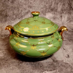 Könnte beinhalten: Eine grüne Keramikservierplatte mit goldenem Deckel und goldenen Verzierungen. Die Platte hat ein dekoratives Muster aus goldenen Sternen und Linien.