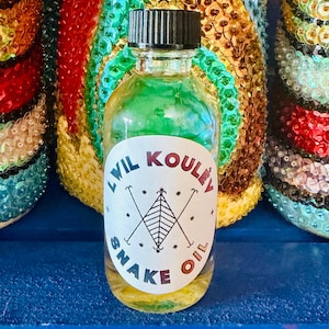 Può includere: Una piccola bottiglia di vetro trasparente con tappo nero, riempita di liquido verde. L'etichetta bianca riporta la scritta "Lwil Kouley Snake Oil" e un disegno. Lo sfondo presenta decorazioni colorate con paillettes.