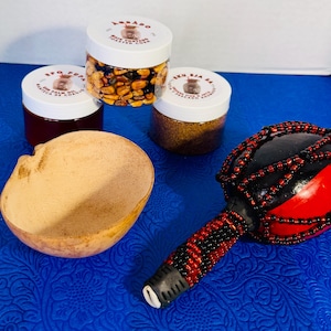 May include: A selection of items on a blue surface, including a gourd bowl, a beaded maraca with red and black accents, and several jars with white lids. The jars contain various grains and seeds.