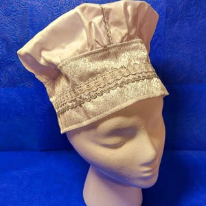 May include: White satin chef hat with a silver lace trim. The hat is on a white mannequin head.