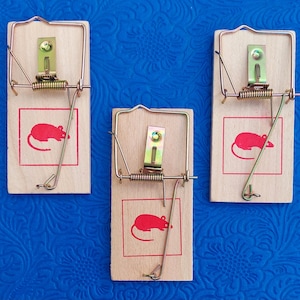 May include: Three wooden mouse traps with a spring-loaded bar and a red mouse silhouette. The traps are on a blue background.