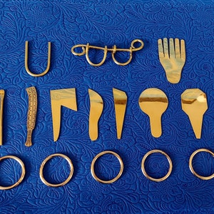 May include: A set of 12 gold-toned metal objects, including a U-shaped piece, a ring, a small comb, a spoon, a knife, and six small rings. The objects are arranged on a blue patterned surface.