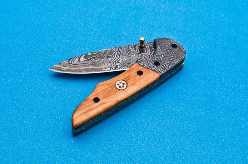 May include: A folding pocket knife with a wood handle and a patterned steel blade. The blade is partially open and the handle has a small red and gold design.