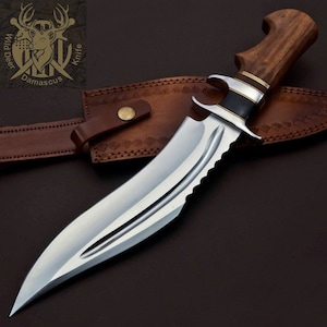 May include: A large, silver, serrated knife with a brown wooden handle. The knife is in a brown leather sheath with a brass button.