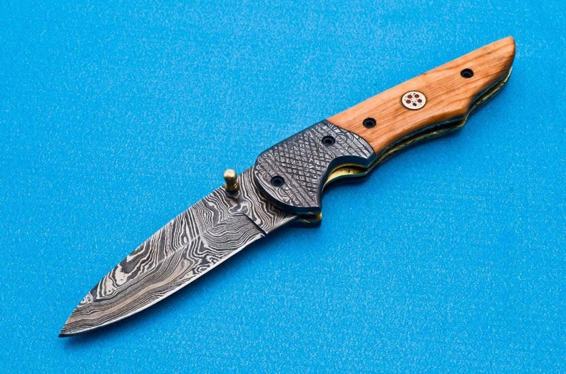 May include: A folding pocket knife with a wood handle and a patterned steel blade. The handle is brown with a red and white design. The blade is silver with a wavy pattern.