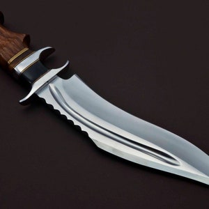 May include: A large, silver-colored hunting knife with a wooden handle. The handle is dark brown with a gold band around it. The blade has a serrated edge and a pointed tip.