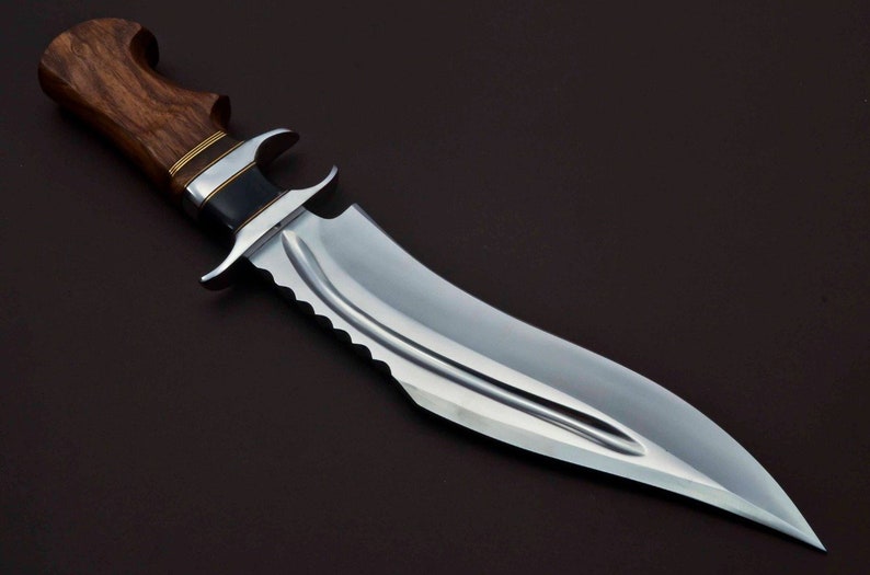 May include: A large, silver-colored hunting knife with a wooden handle. The handle is dark brown with a gold band around it. The blade has a serrated edge and a pointed tip.