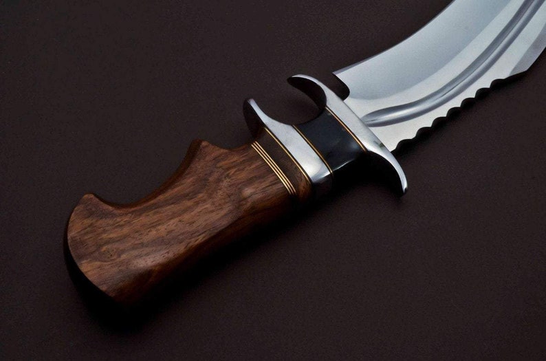 May include: A close-up of a hunting knife with a brown wooden handle and a silver blade. The blade has a serrated edge and a black and silver accent near the handle.
