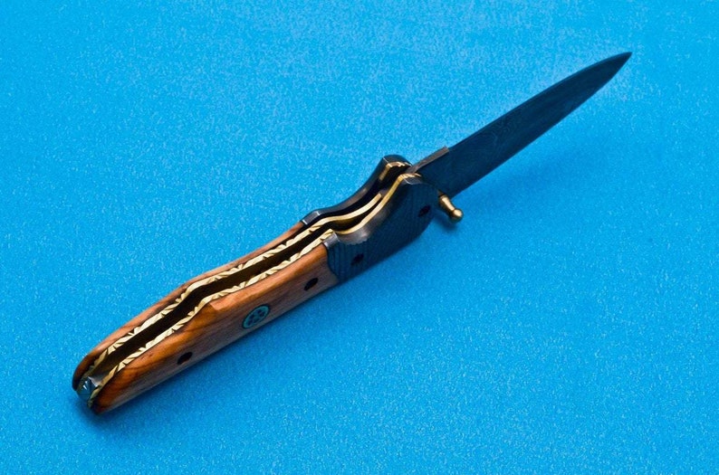 May include: A folding knife with a wooden handle and a black blade. The handle has a gold inlay design.