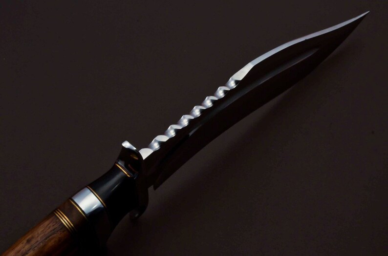 May include: A close-up of a hunting knife with a wooden handle and a serrated blade. The blade is made of stainless steel and has a black finish.