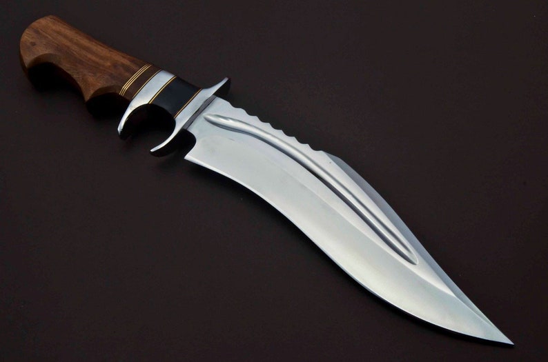 May include: A large, silver, curved knife with a wooden handle. The handle has a black and gold inlay. The blade has a serrated edge and a single fuller.