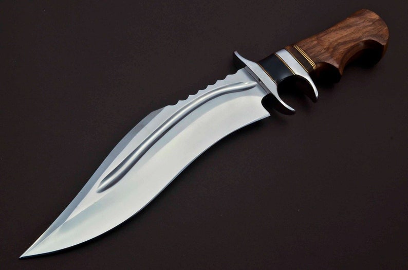 May include: A silver-colored hunting knife with a brown wooden handle. The blade has a serrated edge and a curved shape.