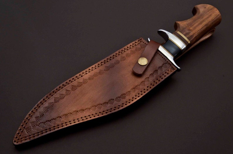 May include: A brown leather sheath with decorative stitching and a brass button. A hunting knife with a wooden handle is inside the sheath.