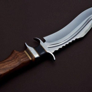 May include: A silver knife with a curved blade and a wooden handle. The blade has a serrated edge and a black accent near the handle.