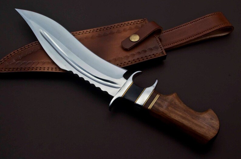 May include: A curved, silver-colored knife with a wooden handle and a leather sheath. The knife has a serrated edge and a decorative metal band around the handle.