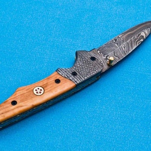 May include: A folding knife with a wooden handle and a patterned steel blade. The handle has a red and white design.