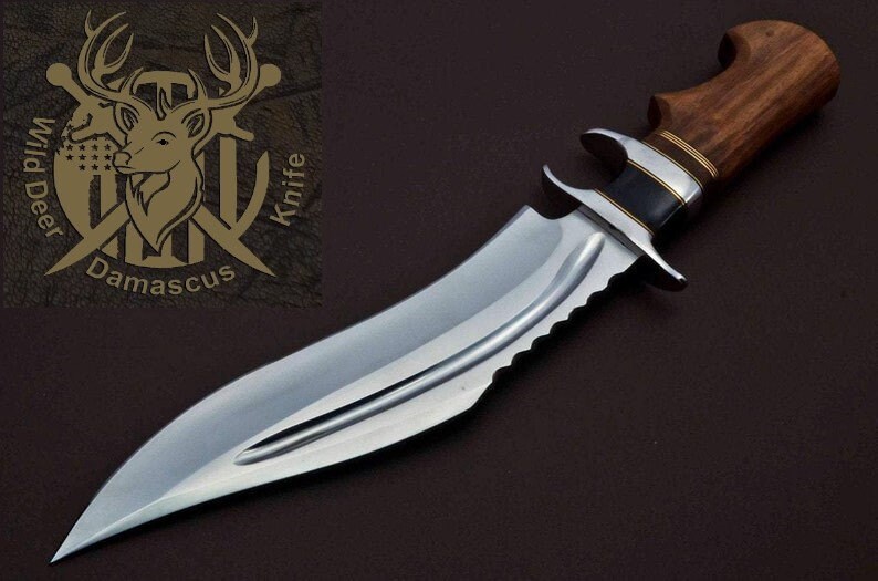 May include: A silver hunting knife with a brown wooden handle and a serrated edge. The knife has a brass accent on the handle and a black accent on the blade. The knife is on a brown background. The text "Wild Deer Knife Damascus" is visible in the upper left corner of the image.