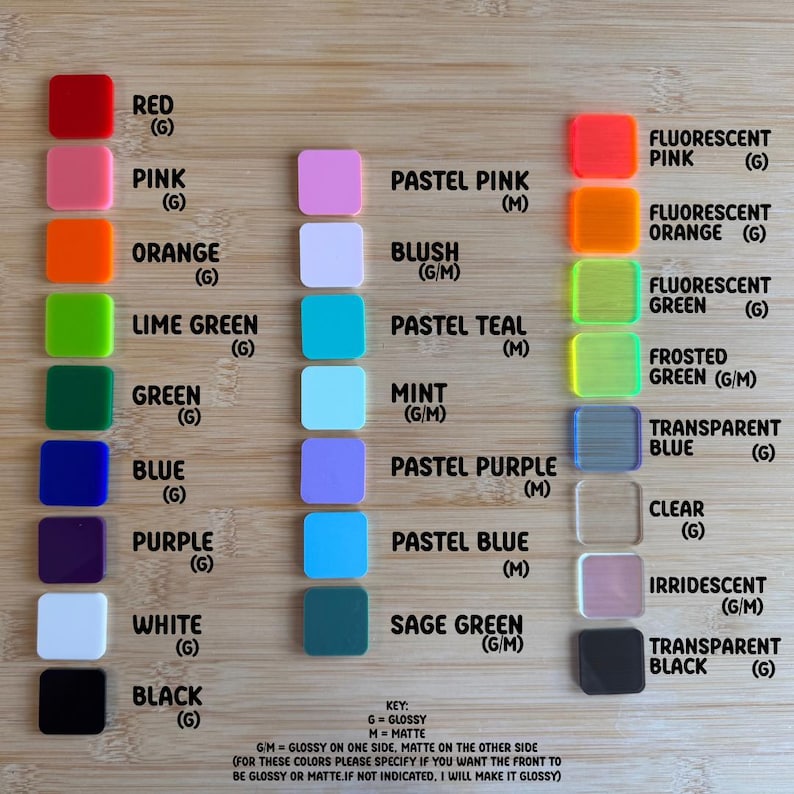 May include: A wooden surface displays a color chart of square acrylic pieces. Colors include red, pink, orange, lime green, green, blue, purple, white, and black, with fluorescent and pastel shades. The key indicates glossy or matte finishes.