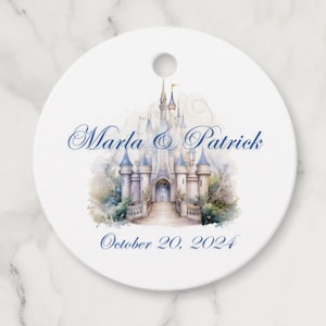 May include: A white round wedding favour tag with a watercolour illustration of a fairytale castle. The text "Marla & Patrick" and "October 20, 2024" is printed in blue.