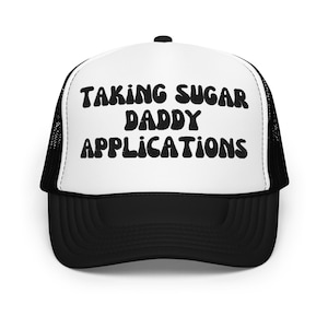 May include: A black and white trucker hat with a white front panel and a black mesh back. The front panel has the text "TAKING SUGAR DADDY APPLICATIONS" in black bubble letters.