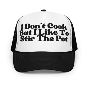 Pode incluir: Um boné de caminhoneiro preto e branco com um painel frontal branco e uma parte de trás de malha preta. O painel frontal tem o texto "I Don't Cook But I Like To Stir The Pot" em preto.