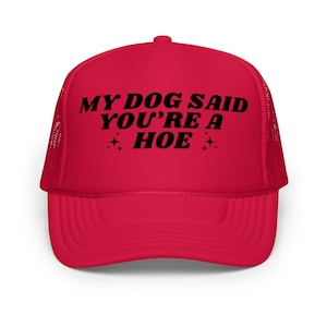 Puede incluir: Gorra de camionero roja con visera curva y parte trasera de malla. La gorra presenta el texto "MY DOG SAID YOU'RE A HOE" en negro, con estrellas. Un accesorio divertido.