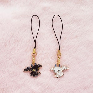 May include: Two black and white dragon phone charms with gold accents. The charms are attached to black cords.