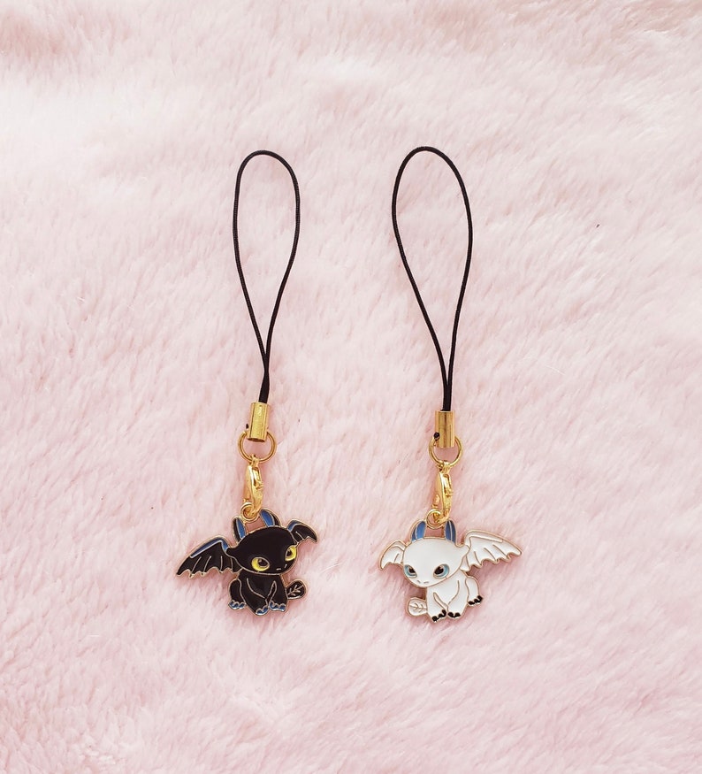May include: Two black and white dragon phone charms with gold accents. The charms are attached to black cords.