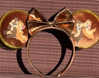 May include: Brown velvet Minnie Mouse ears with a gold bow and a printed image of Chip and Dale hugging.
