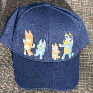 May include: A navy blue baseball cap with a colorful cartoon design featuring four dogs. The dogs are wearing different colored shirts and are in various poses.