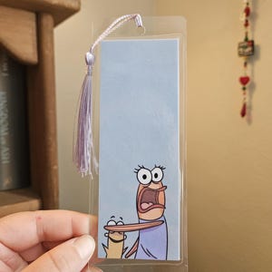 Peut inclure: Marque-page rectangulaire avec une illustration de dessin animé de deux poissons aux expressions surprises. Le marque-page a un fond bleu clair et un pompon violet. Le marque-page est enfermé dans une pochette en plastique transparent.
