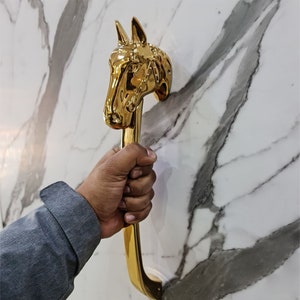 以下が含まれることがあります： 馬の頭の形をした金色のドアノブ。ノブは白い大理石の壁に取り付けられています。