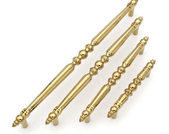 May include: Set of four gold-colored cabinet pulls with ornate detailing. The pulls feature a combination of straight bars and decorative, beaded sections. The hardware is designed for furniture and cabinetry, offering a classic aesthetic.