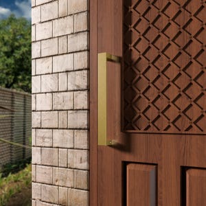 May include: A close-up of a wooden door with a gold-colored rectangular handle. The door has a decorative geometric pattern and is next to a brick wall. The door is made of dark brown wood.