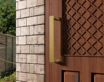 May include: A close-up of a wooden door with a gold-colored rectangular handle. The door has a decorative geometric pattern and is next to a brick wall. The door is made of dark brown wood.