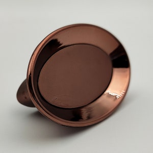Puede incluir: Un plato ovalado de cobre con un borde elevado. El plato tiene una superficie lisa y brillante.