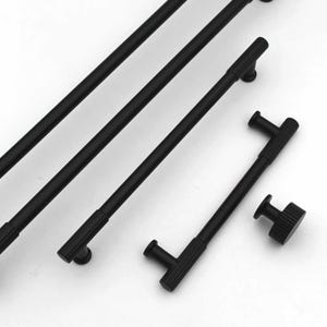 May include: A selection of black cabinet handles and knobs. The handles are long and cylindrical with a ribbed texture, and the knobs are round with a similar ribbed design. The hardware is set against a white background.