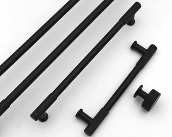May include: A collection of black cabinet pulls and knobs. The pulls are long and cylindrical with a ribbed texture, and the knobs are round with a similar ribbed design. The hardware is set against a white background.