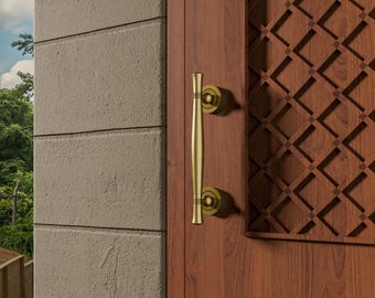 May include: A close-up of a wooden door with a decorative brass handle. The door is a warm brown color, and the handle is a long, vertical bar with circular accents. The door also features a decorative carved panel.