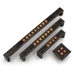 Könnte beinhalten: Ein Set aus vier bronzefarbenen Möbelbeschlägen. Das Set umfasst drei rechteckige Griffe in verschiedenen Längen und einen quadratischen Knauf. Jedes Stück hat ein Mosaik aus kleinen schwarzen Quadraten und eine zentrale Reihe goldfarbener quadratischer Akzente.