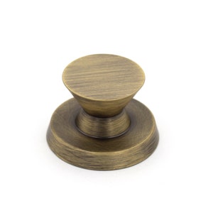 May include: A bronze cabinet knob with a circular top and base, joined by a conical section. The knob has a textured, aged appearance, suggesting a vintage style. The hardware is designed for use on drawers or cabinets.