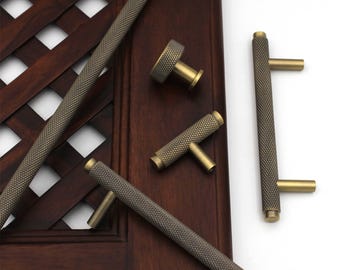 May include: An assortment of antique brass cabinet hardware, including handles and knobs. The hardware features a textured, diamond-patterned grip and a brass finish. The pieces are arranged on a dark wood surface, showcasing their design and style.